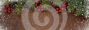 Pine branches with red berries on a wooden background. Christmas snowy background. Happy New Year! Banner.Copy space for your text