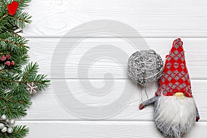 Pine branches with snowflake and mitten ornaments, New Year gnome with silver ball on white wooden background