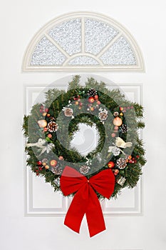 Pine Christmas Wreath with Red Bow Hanging on White Door