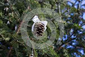 Pine cone with a white satin bow in a fir tree with blue sky in the background, organic christmas decorations concept