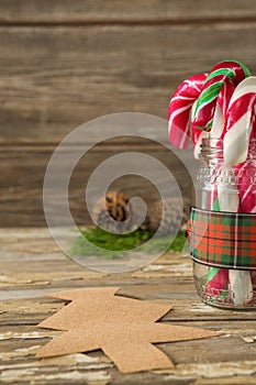 Pine cones and candy cane in jar against wooden plank