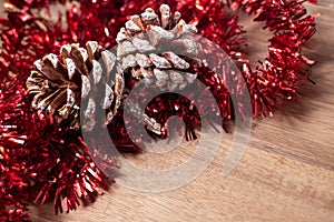 Pine cones and red christmas tinsel on wooden background