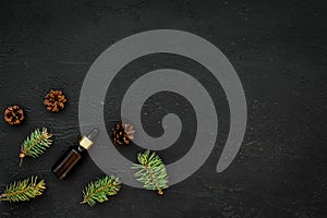 Pine essential oil in bottles on black background top view. Pattern with pine branch and cone copy space