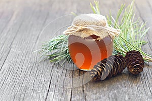 Pine honey in jar or bowl with honey stick and pine cones on wooden rustic table