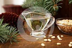 Pine nut oil and bowl of pine nuts on wooden background with cones, cedar brunches