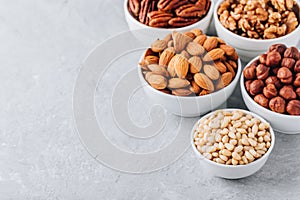 Pine nuts, almonds, pecans, walnuts and hazelnuts in white bowls on grey background. Mixed nuts. Healthy food and snack.