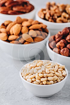 Pine nuts, almonds, pecans, walnuts and hazelnuts in white bowls on grey background. Mixed nuts.