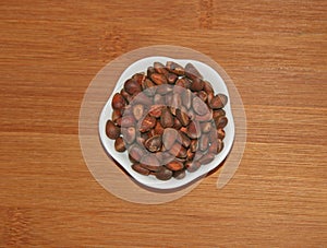 Pine nuts are placed in a small white plate. Brown, beige, white.
