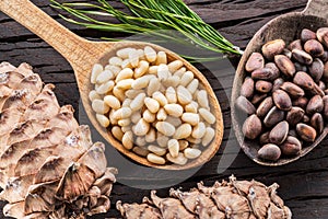 Pine nuts in the spoon and pine nut cone on the wooden table. Organic food