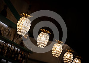 Pineapple beautiful Art Deco crystal glass lights hanging from ceiling over bar illuminated at night with bottles behind