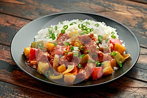 Pineapple and Chicken in sweet and sour sauce with bell pepper, rice and spring onion in black plate