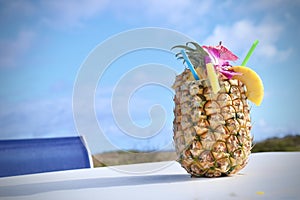 Pineapple cocktail on white table against blue sky background.