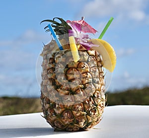 Pineapple cocktail on white table against blue sky background.
