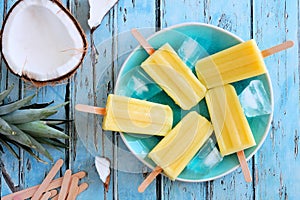 Pineapple coconut popsicles, top view scene on blue wood