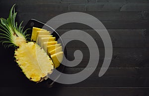 Pineapple cut in black bowl on dark wooden background. Copy space