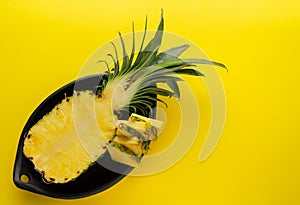 Pineapple cut in black ceramic bowl on yellow background. Top view