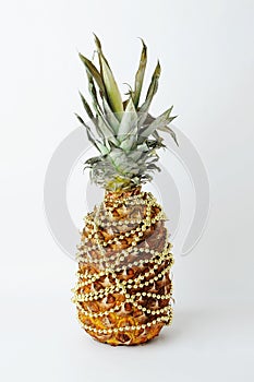 Pineapple decorated like a Christmas tree. Gold beads garland. White background