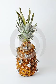 Pineapple decorated like a Christmas tree. Little silver shiny balls. White background