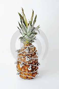 Pineapple decorated like a Christmas tree. Silver beads and balls. White backgroumd