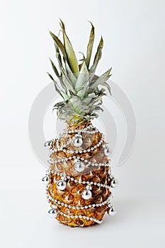 Pineapple decorated like a Christmas tree. Silver beads and balls. White backgroumd