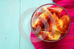 Pineapple cutted with chili powder and piquant sauce in glass on turquoise background