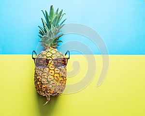 Pineapple fruit in sun glasses on blue-and-yellow background