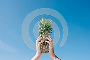 Pineapple in hands on blue sky background