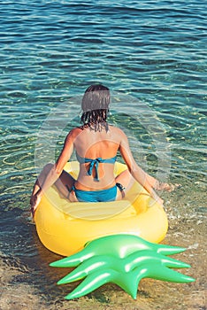 Pineapple inflatable mattress, activity and joy. Summer vacation and travel to ocean. Girl sunbathing on beach with air