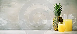 Pineapple juice in glassware and whole pineapple fruit on gray background. Copy space, sunlight effect. Summer, holiday photo