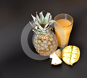 Pineapple juice with the mango in a tall faceted glass on a black background, next to pieces of tropical fruits
