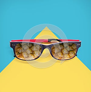 Pineapple reflection in round sunglasses on bright blue and soft yellow background.