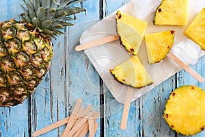 Pineapple slice popsicles, top view over blue wood