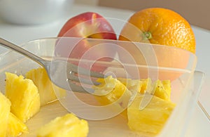 Pineapple slices in a plastic can, a metal fork, orange and nectarine.