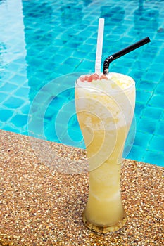 Pineapple smoothie in tall glass with swimming pool background.