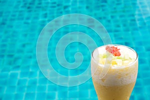Pineapple smoothie in tall glass with swimming pool background.