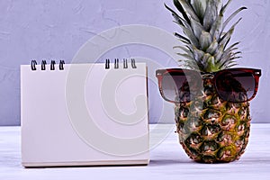 Pineapple in sungasses and blank paper notepad.