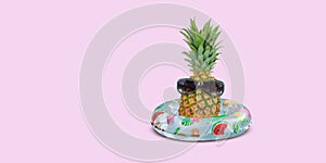 Pineapple with sunglasses in inflatable swim ring on pink background.