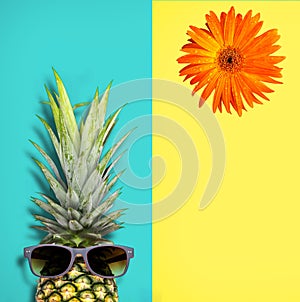 Pineapple with sunglasses and orange flower on light green and soft yellow background.