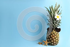 Pineapple with sunglasses, plumeria flower and starfishes on light blue background, space for text. Creative concept