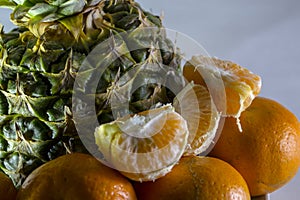 Pineapple and tangerines on a white plate close-up.