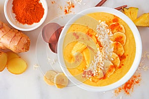 Pineapple, turmeric and ginger smoothie bowl. Top view scene on a white marble background.