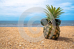 Pineapple wearing sunglasses on the sand with turquoise sea