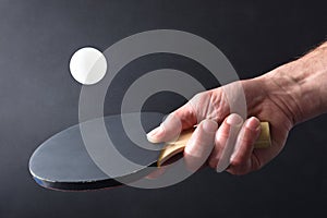 Ping-pong player hitting ball with paddle on black isolated background