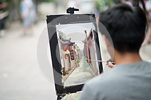 Pingyao, China - 08 14 2016: A chinese man painting in a street with traditional houses and red lanterns in Pingyao. Shanxi, China