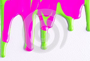 Pink abd green liquid drops of paint color flow down on white canvas. Abstract Colorful paint dripping on the white wall with