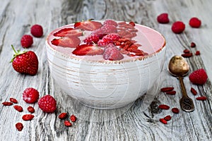 Pink acai, maca powder smoothie bowl topped with sliced strawberries, raspberries and goji berries. photo