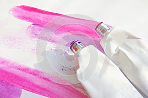 Pink acrylic paints tubes and hand drawn abstract magenta watercolor drawing picture on white textured paper background