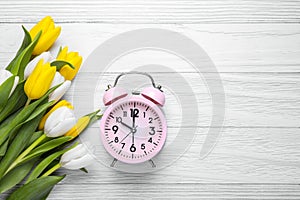 Pink alarm clock and beautiful tulips on white wooden table, flat lay with space for text. Spring time