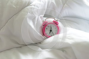 Pink Alarm clock get up six oâ€™clock on bed in morning with sun light.