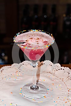 pink alcohol cocktail in glass with high leg with black straw on white napkin in restaurant